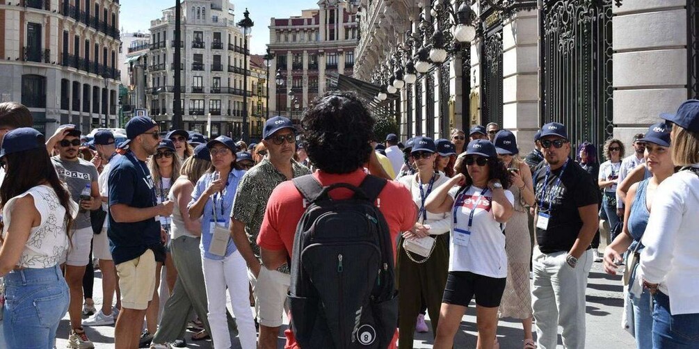 A crowded street with people standing and walking, historic buildings, and ornate street lamps. 2
