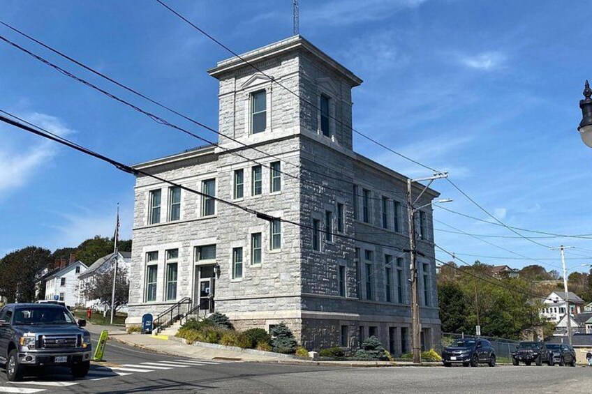 A large stone building with a tower, a street with cars, and a clear blue sky. 1