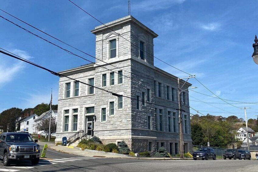 A historic stone building with a tower, located at a street corner with cars and a pedestrian crossing. 1