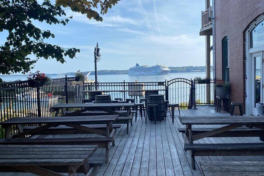 A wooden deck with tables and chairs overlooking a body of water with a cruise ship in the distance. 3