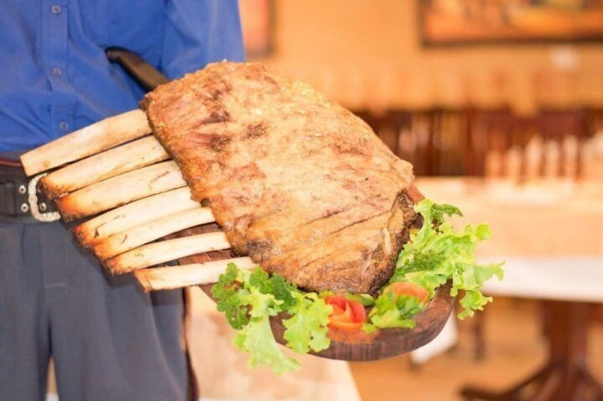 Una persona lleva una gran carne a la parrilla sobre una tabla de madera, acompañada de lechuga y tomates. 2