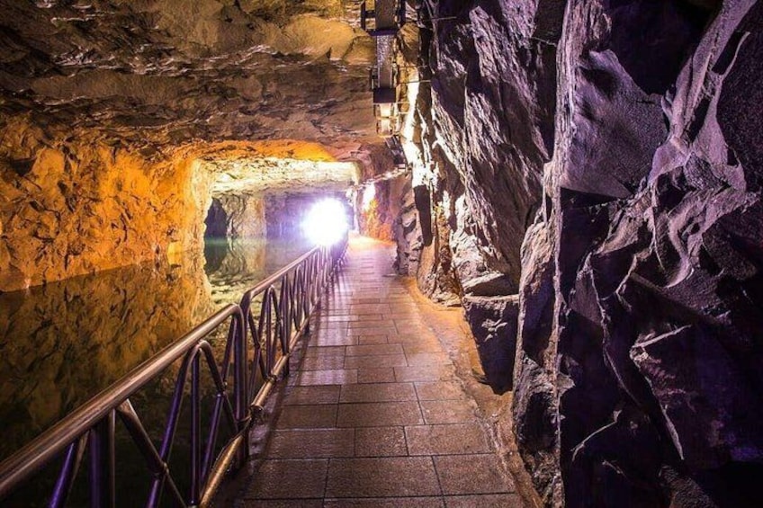 A stone staircase in a cave with a metal railing, leading to a brighter area. 1