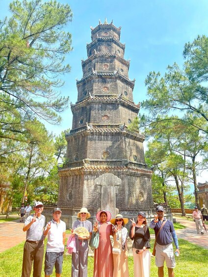 A group of people standing in front of a multi-tiered pagoda-like structure with a clock on the top. 5