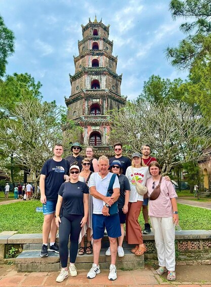 A group of people posing in front of a multi-tiered pagoda-like structure in a park with trees. 4