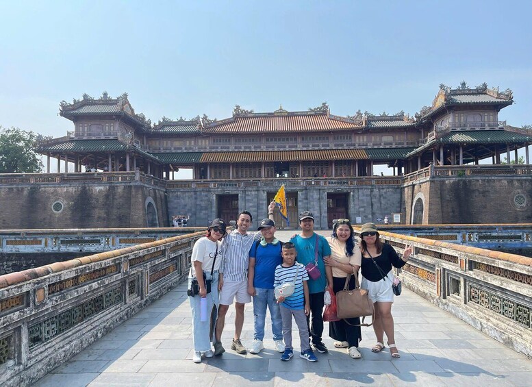 A group of people posing in front of a traditional Chinese building with ornate roofs and a stone wall. 2