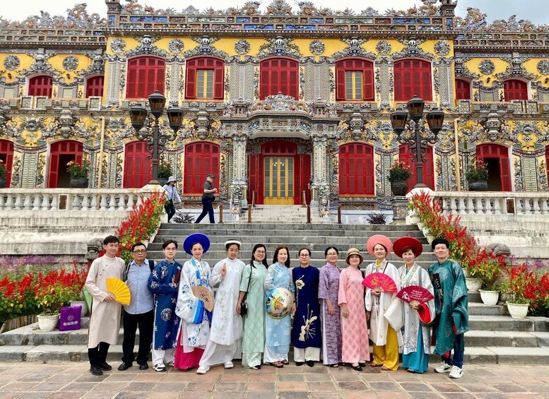 A group of people in traditional attire standing in front of a richly decorated building with red doors and intricate patterns. 1