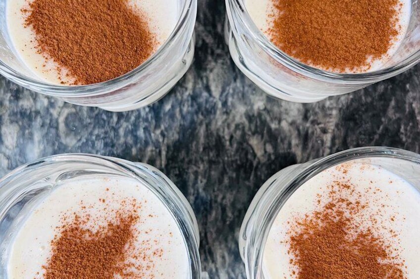 Four glass cups with a white creamy substance and a brown powder on top, placed on a textured surface. 4