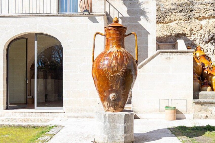 A large, ornate ceramic vase on a pedestal in front of a building with a stone facade and a glass door. 2