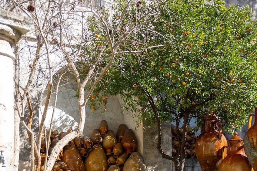 A tree with green leaves and orange fruits, a stone wall, and several large ceramic pots. 3