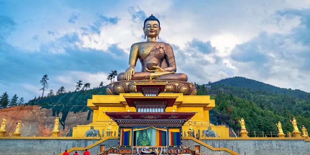A large seated Buddha statue on a pedestal with a colorful shrine in front, set against a mountainous backdrop. 4