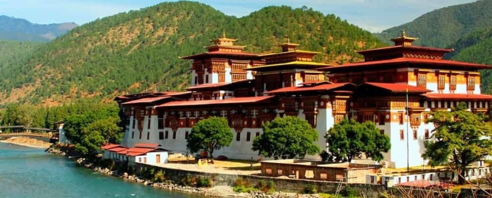 A traditional multi-tiered building with red and white walls, surrounded by lush greenery and mountains. 2