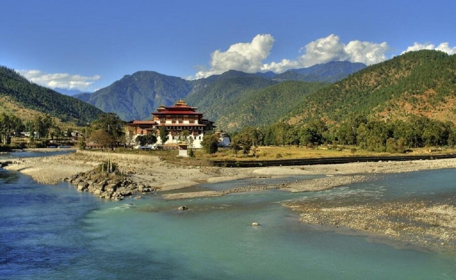 A traditional building by a river with mountains in the background. 1