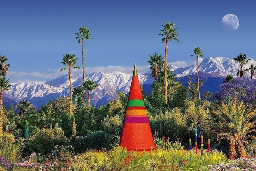 Una estructura cónica y colorida en un jardín con palmeras y una cadena montañosa al fondo. 1