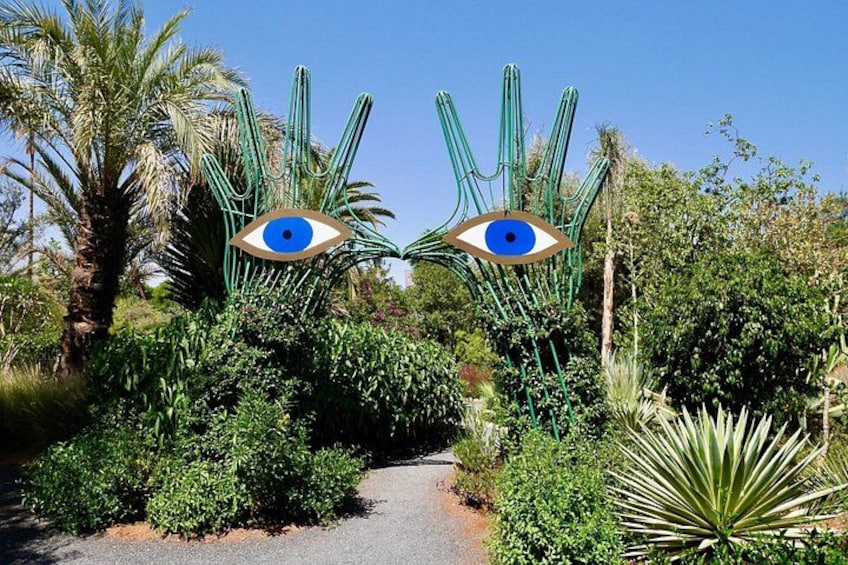 A pathway flanked by cacti and a blue eye-shaped sculpture. 3