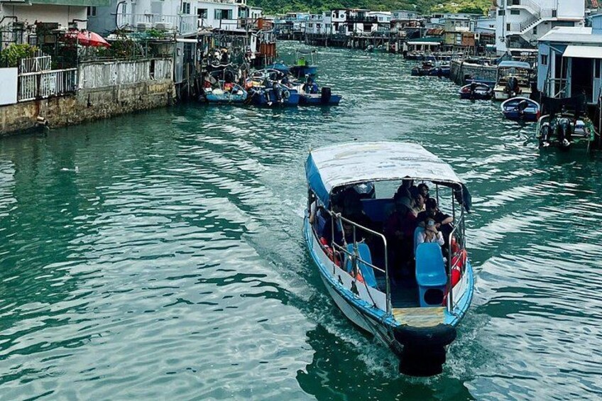 Una embarcación con pasajeros navegando por una vía fluvial bordeada de edificios y otras barcas. 2