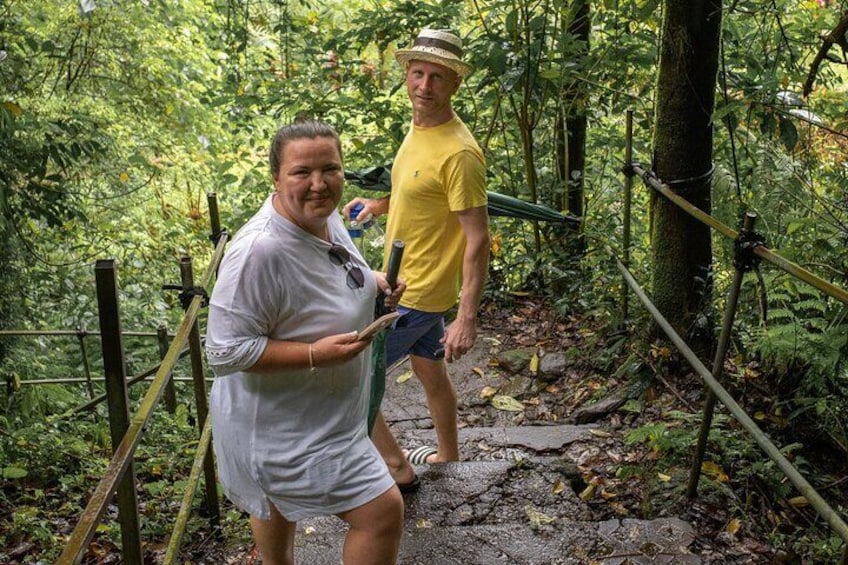 Two people on a forested trail with wooden railings and a stone path. 3