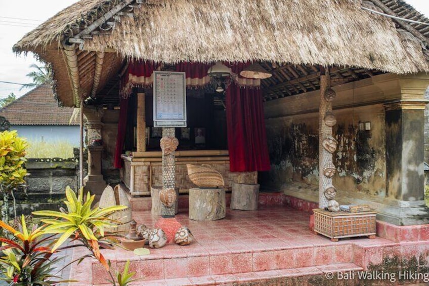 A traditional Balinese house with a thatched roof, a red curtain, and a stone altar. 5
