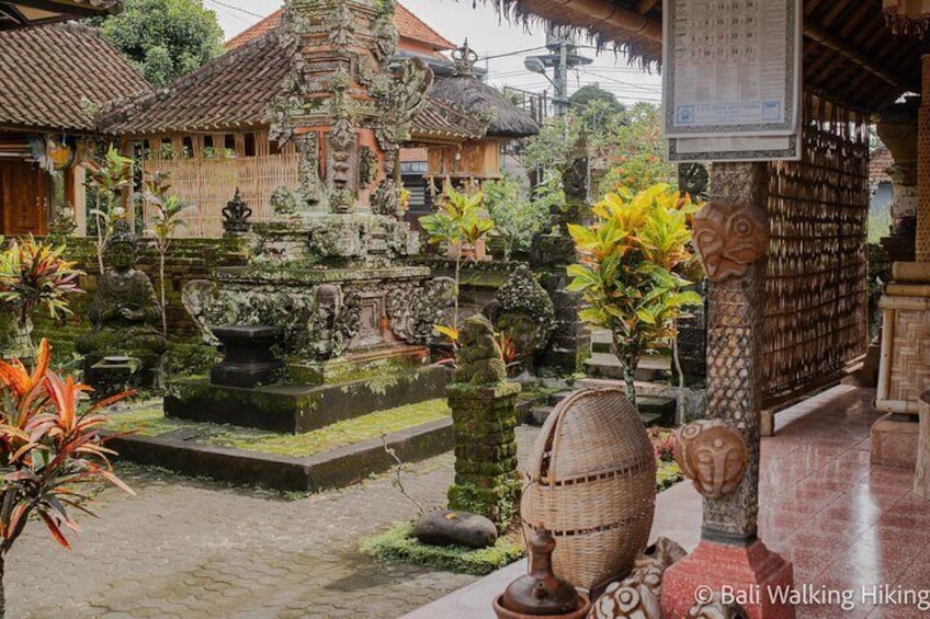 A traditional Balinese temple courtyard with a central water feature, stone statues, and a thatched-roof structure. 4