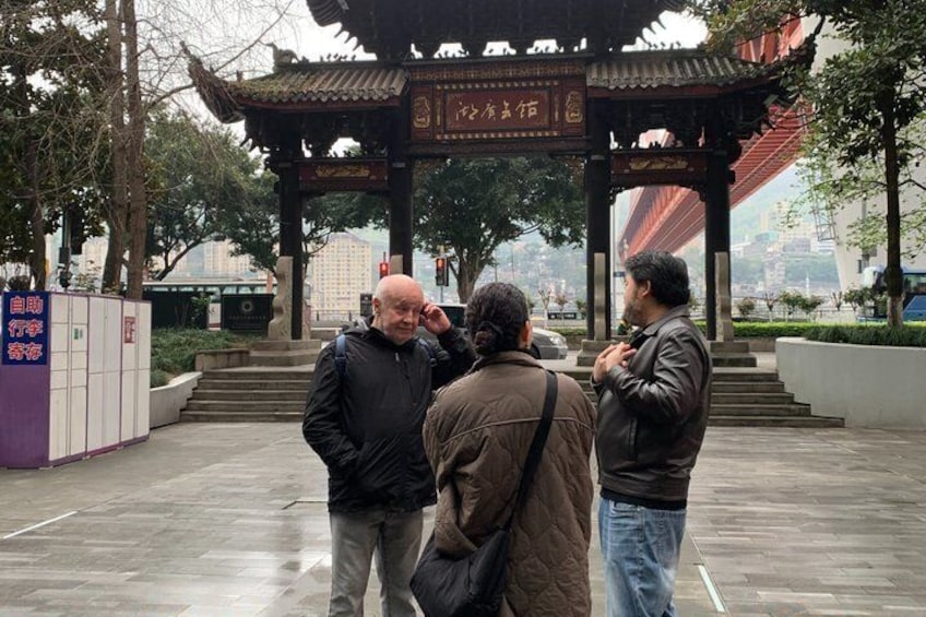 Ein traditioneller chinesischer Pavillon mit Inschriften, nasser Pflasterung und einer Stadtlandschaft im Hintergrund. 4