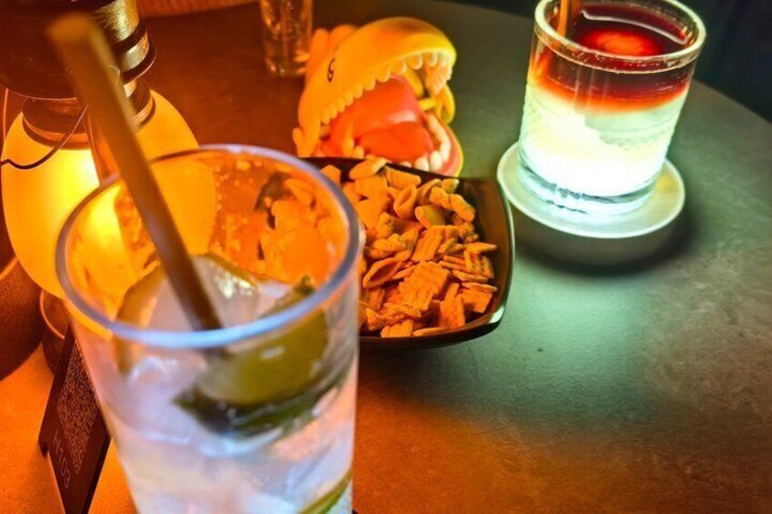 Ein Glas Eistee mit Strohhalm, eine kleine Schale mit Snacks und ein Schnapsglas mit einem schichtartigen Getränk. 5