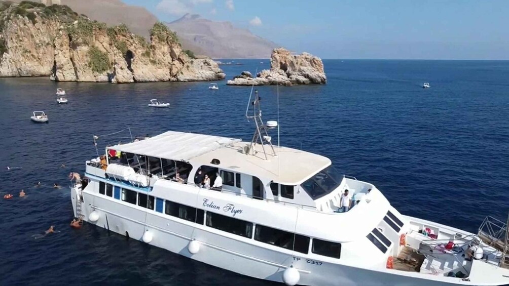 A white boat named 'Colonial Flyer' on calm waters with rocky cliffs and other boats in the background. 2