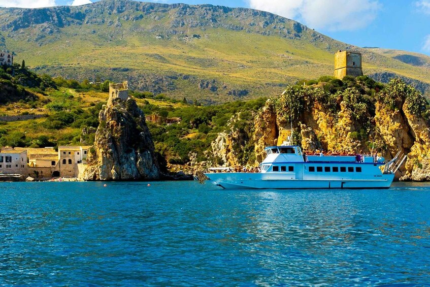 A boat on a calm sea with rocky cliffs and a tower in the background. 1
