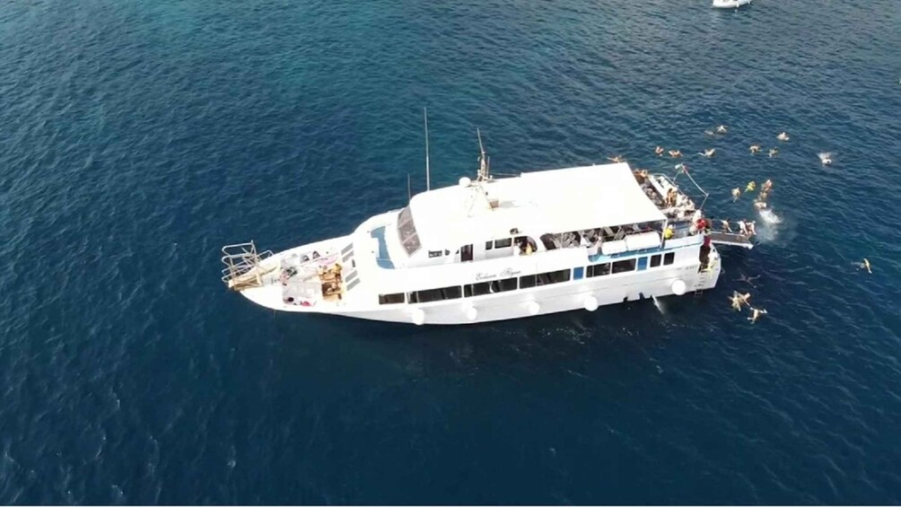 A white boat with multiple decks and passengers, floating on a calm sea. 3