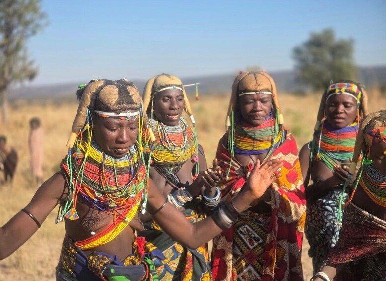 A group of people in traditional attire with colorful bead necklaces and headbands, standing in a grassy field. 5