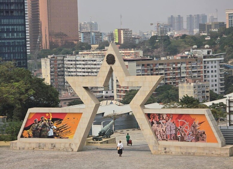 A star monument with murals of soldiers and a cannon, surrounded by urban buildings. 1