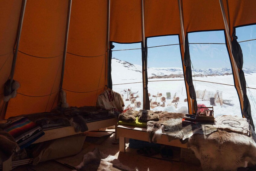 A tent interior with fur items and a snowy landscape visible through the windows. 2