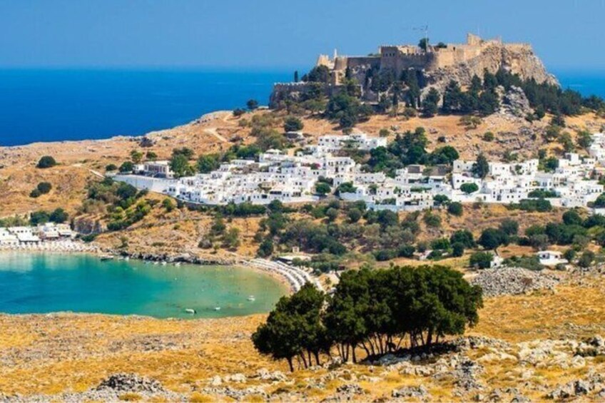 A coastal town with white buildings, a fort on a hill, and a clear blue sea. 1