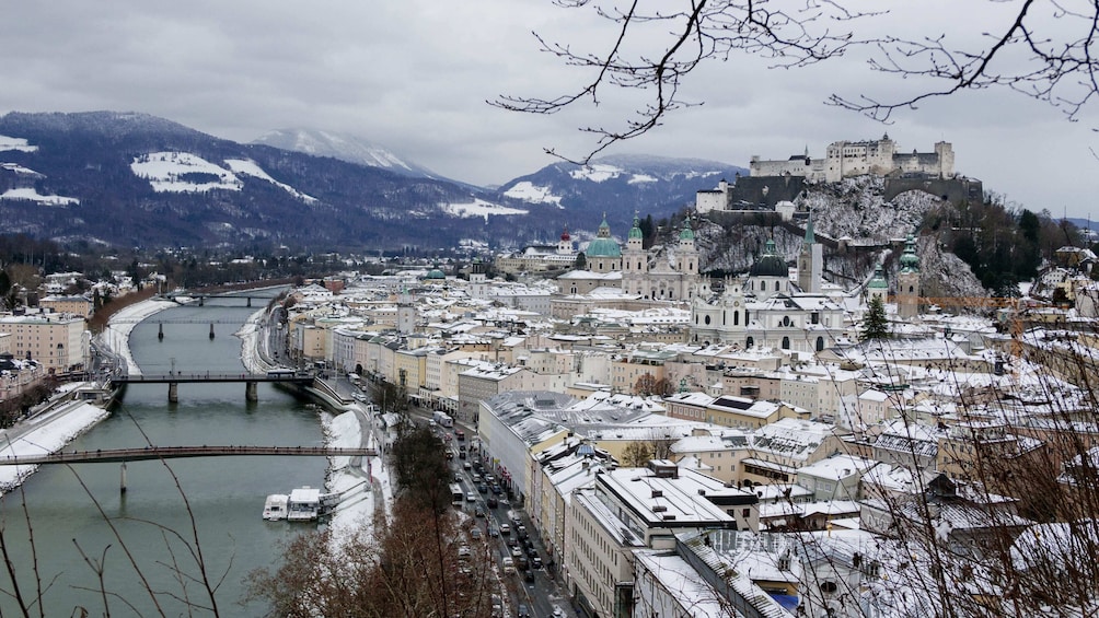 Eine verschneite Stadtansicht mit einem Fluss, einer Brücke und einer Burg auf einem Hügel. 2
