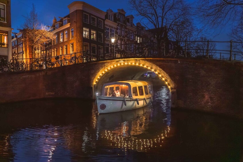 A boat under a lit bridge in a canal with buildings in the background. 2