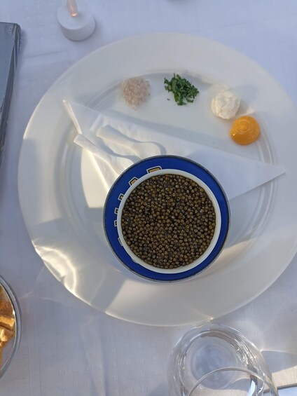 A plate with a blue rim containing black olives, a small pile of green herbs, a dollop of white cream, and a small yellow condiment. 5