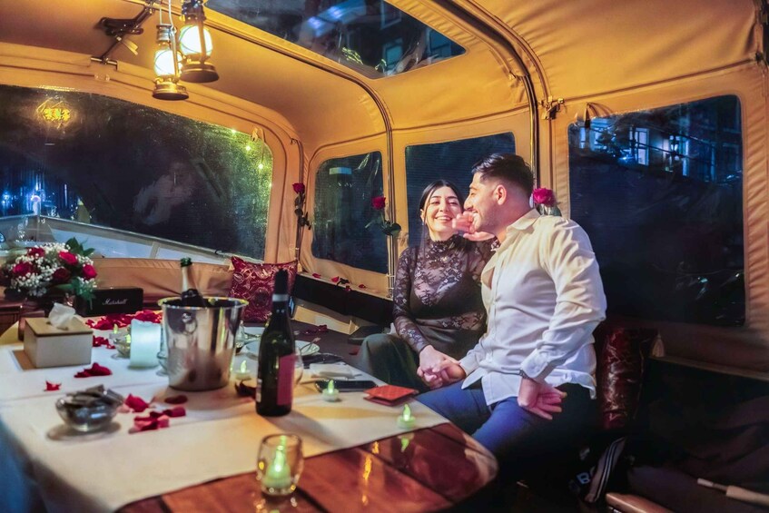 A tent with a table set for two, featuring a bottle of wine, candles, and rose petals. 1