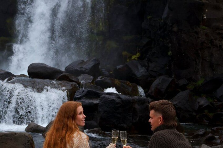 Two people sitting by a waterfall with rocks and water. 2