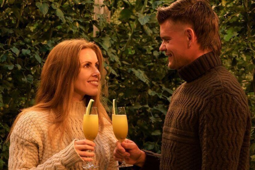 Two people holding glasses of a yellow beverage, standing in front of a leafy background. 5