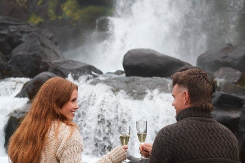 Two people toasting with champagne glasses in front of a waterfall. 1