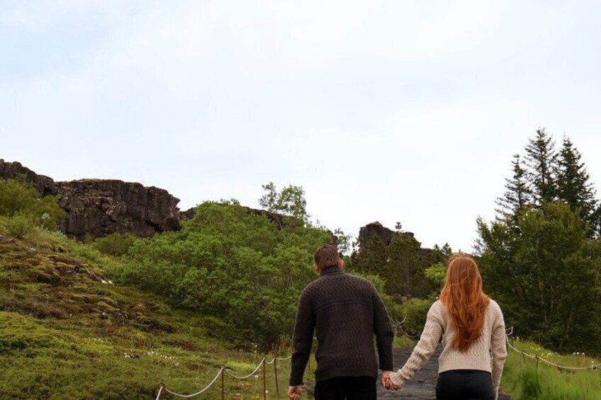 Two people walking on a trail with greenery and rocky terrain. 3