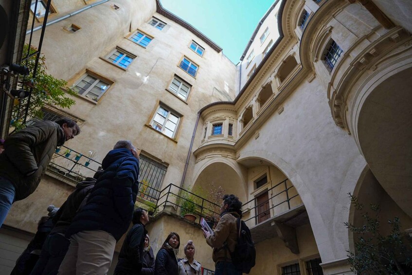 A group of people in an urban courtyard with classical architecture, including arched walkways and balconies. 2