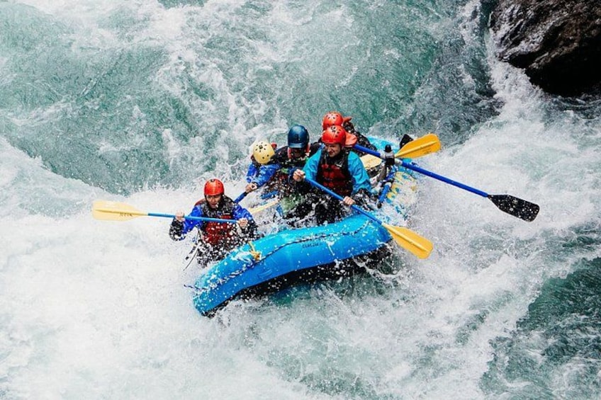 A group of people in a blue raft navigating through a river with rapids. 3