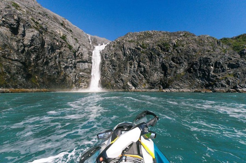 A boat in a turquoise body of water with a waterfall in the background. 5