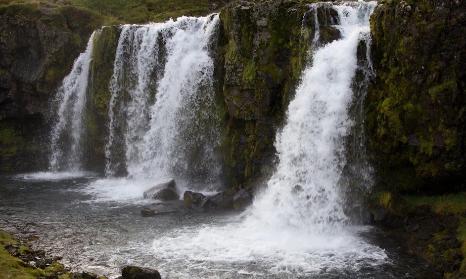 A multi-tiered waterfall surrounded by moss-covered rocks and a flowing river. 5