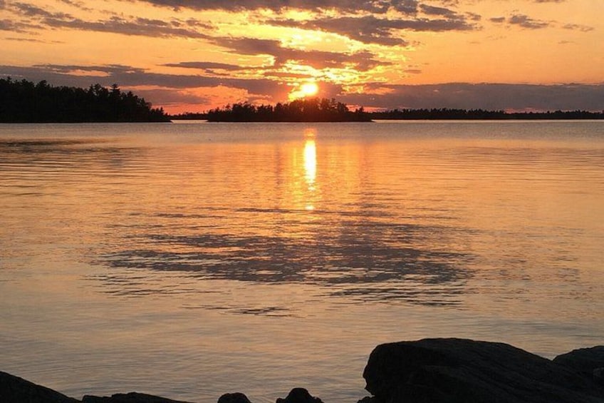 A sunset over a calm lake with a silhouette of trees and rocks in the foreground. 3