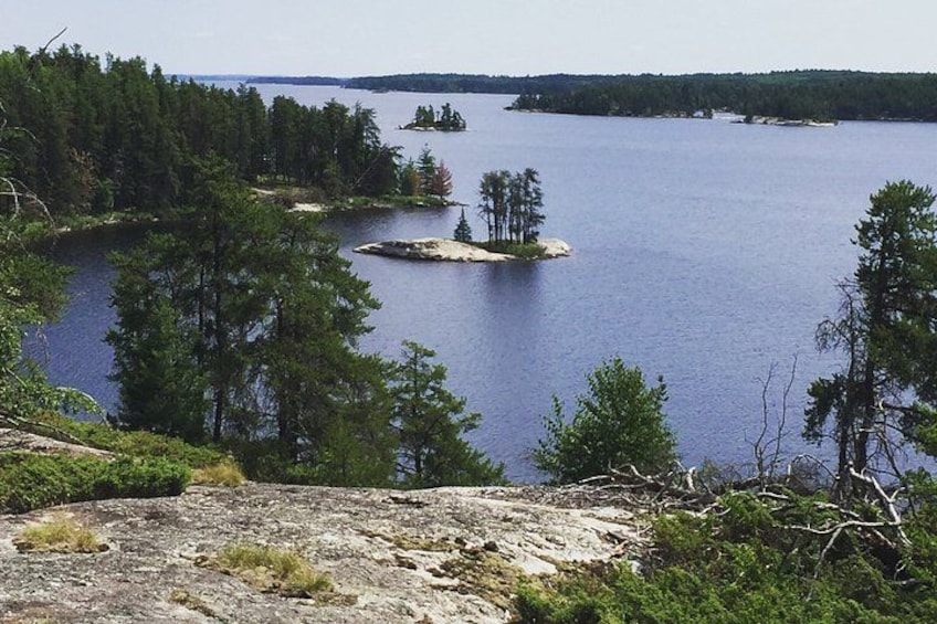En sjö omgiven av tät skog, en stenig strand och en liten ö med träd. 1