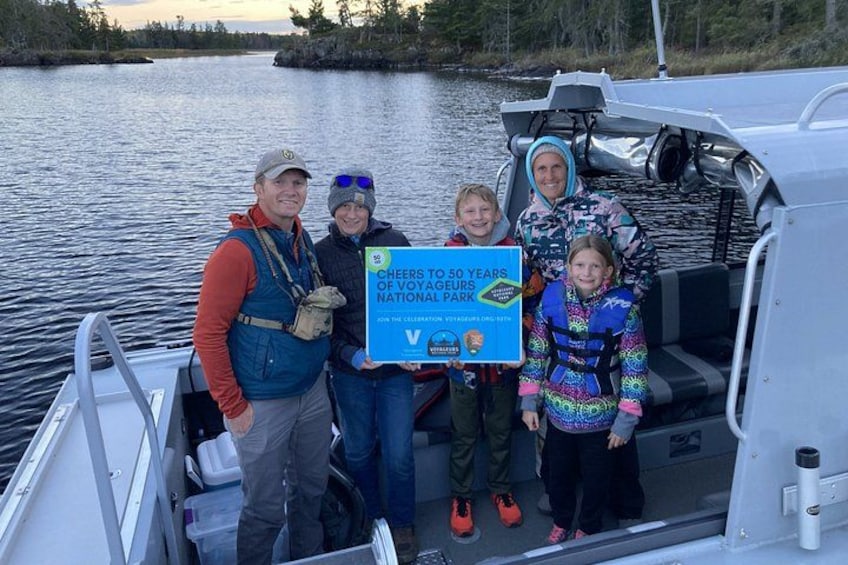 En grupp människor på en båt, med en skylt där det står: ”Grattis till 50 år, Voyageurs nationalpark!” 2