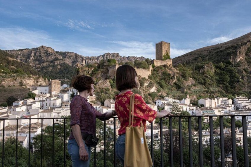 Dos personas contemplan un pueblo con una torre destacada en una colina. 1