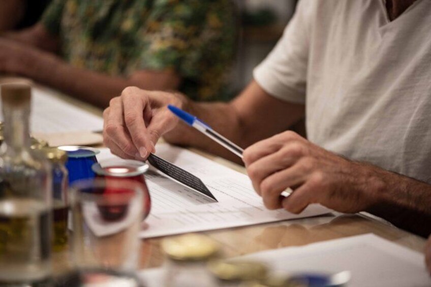 A person writing on a piece of paper with a pen, with a can and a bottle on the table. 4
