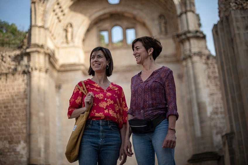 Two people walking in front of a historical building with arched windows and stone columns. 4