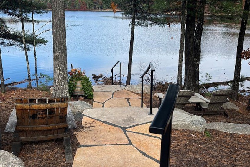 Terraza junto al lago con sillas Adirondack, un banco de madera y un sendero de piedra que conduce a un muelle. 2